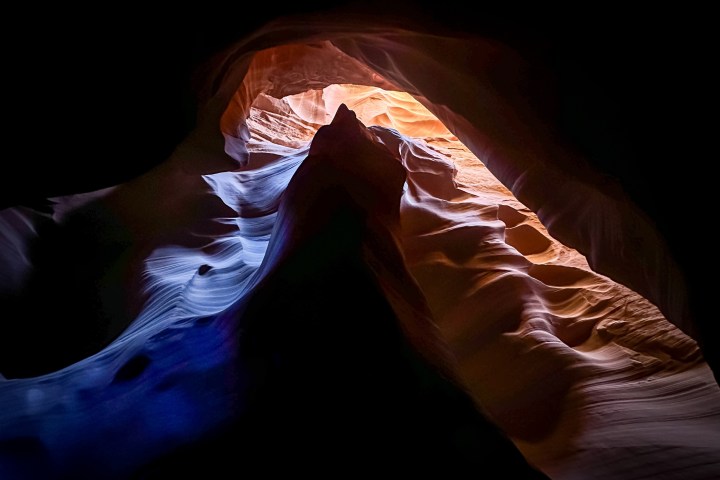 Rock formation in cave with light casting orange and blue hues.