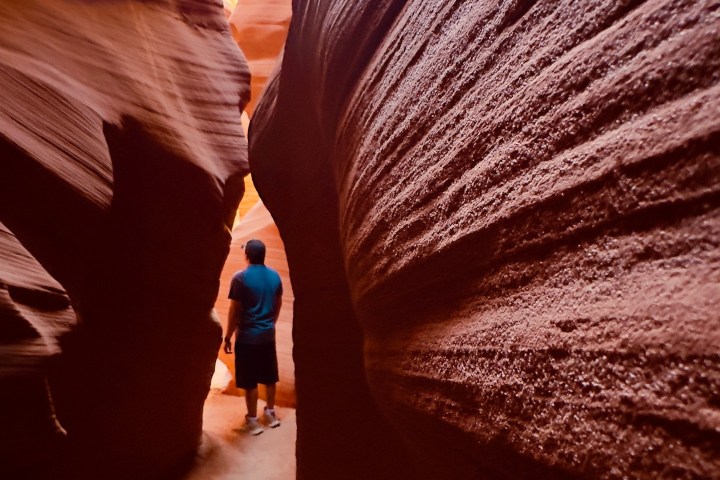Person walking through narrow canyon with textured red rock walls.