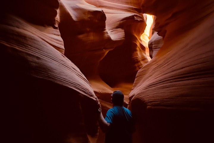 Person in narrow sandstone canyon with glowing light from above.