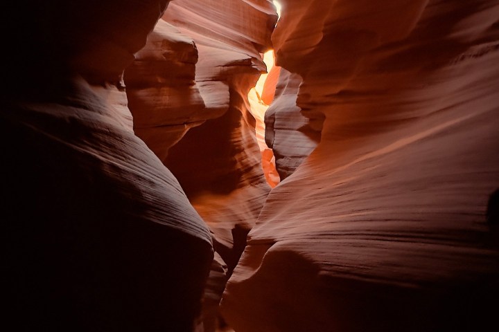 Narrow passage in sandstone canyon with light streaming through openings.