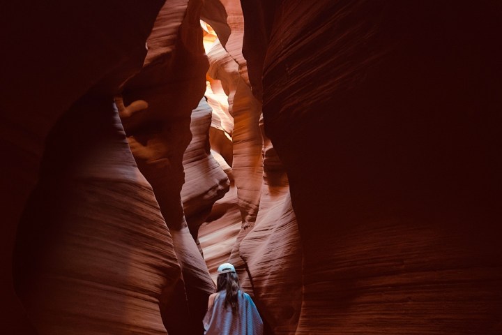 Person walking through narrow sandstone canyon with wavy walls.