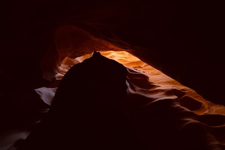 Silhouette of rocks inside a dimly lit cave with light shining through an opening.