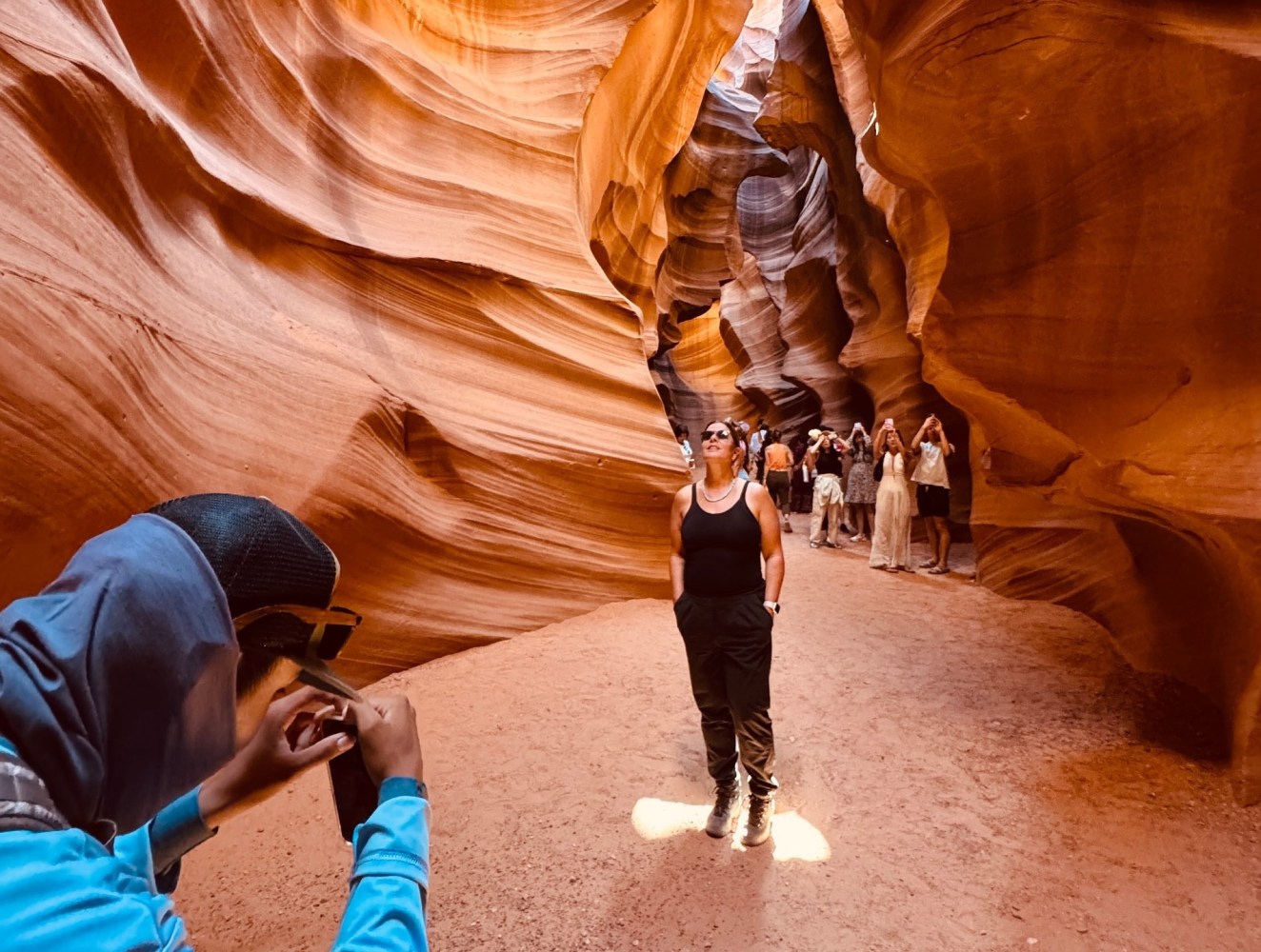 People exploring a sunlit sandstone canyon with smooth, wavy walls.