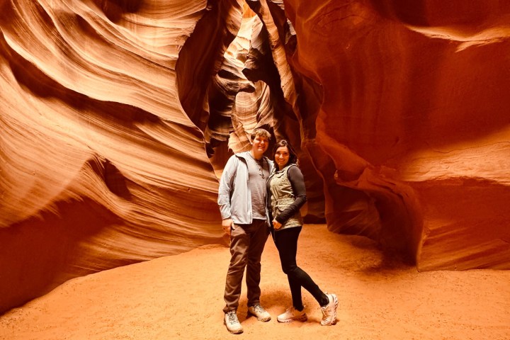 Two people stand in a red rock canyon with swirling walls.