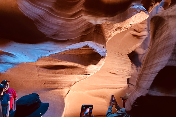 People taking photos in a narrow, illuminated sandstone cave.