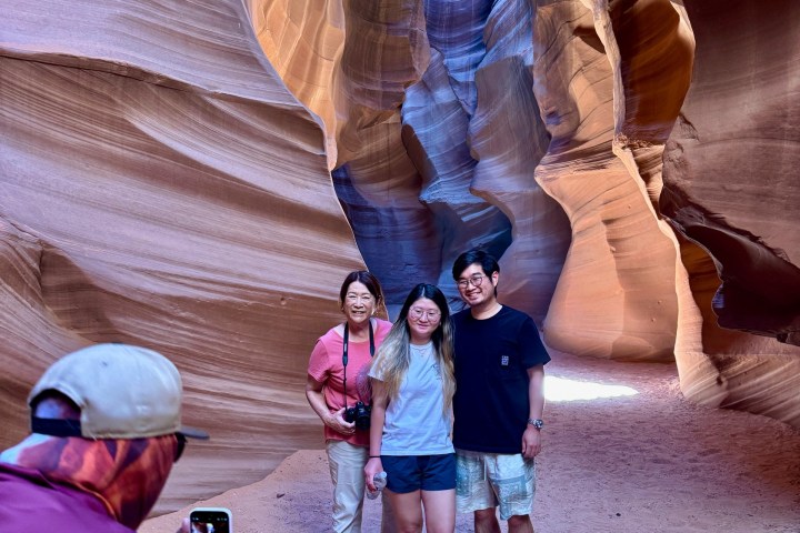 Three people pose in a colorful slot canyon as another person takes a photo.