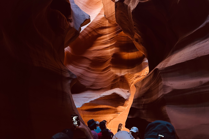 People inside a narrow canyon with wavy, textured walls and overhead light.